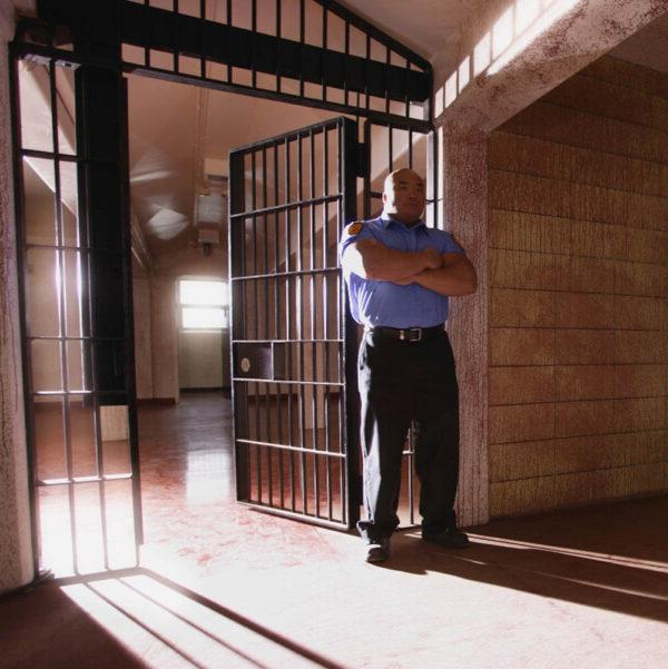 A male corrections officer standing in front of an open cell