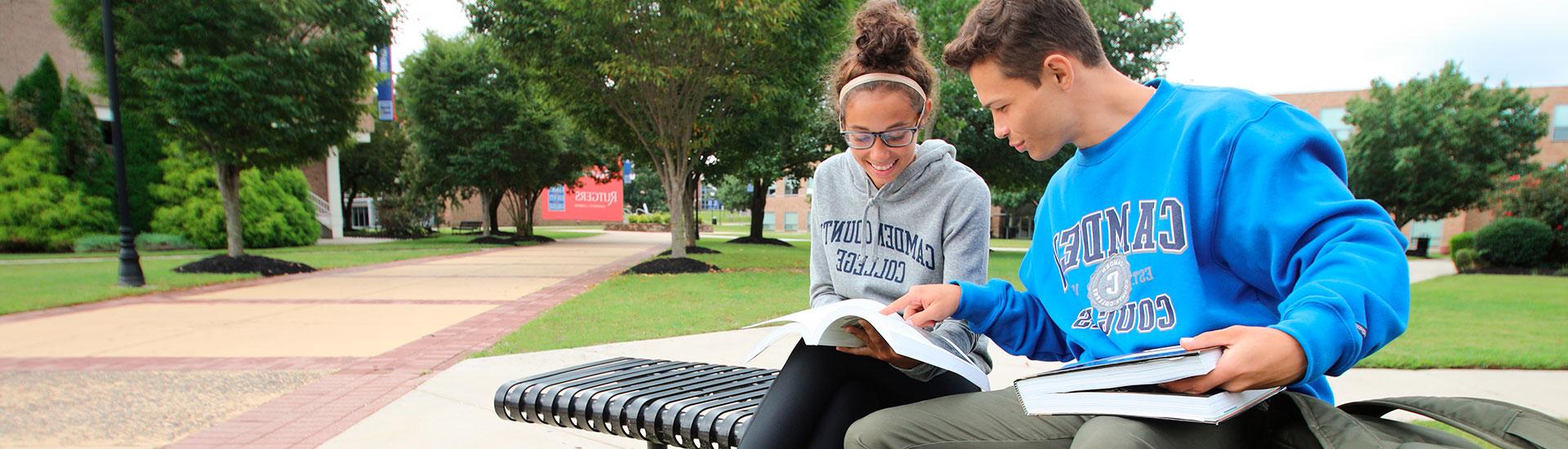 a male and female student sitting on a bench with school books